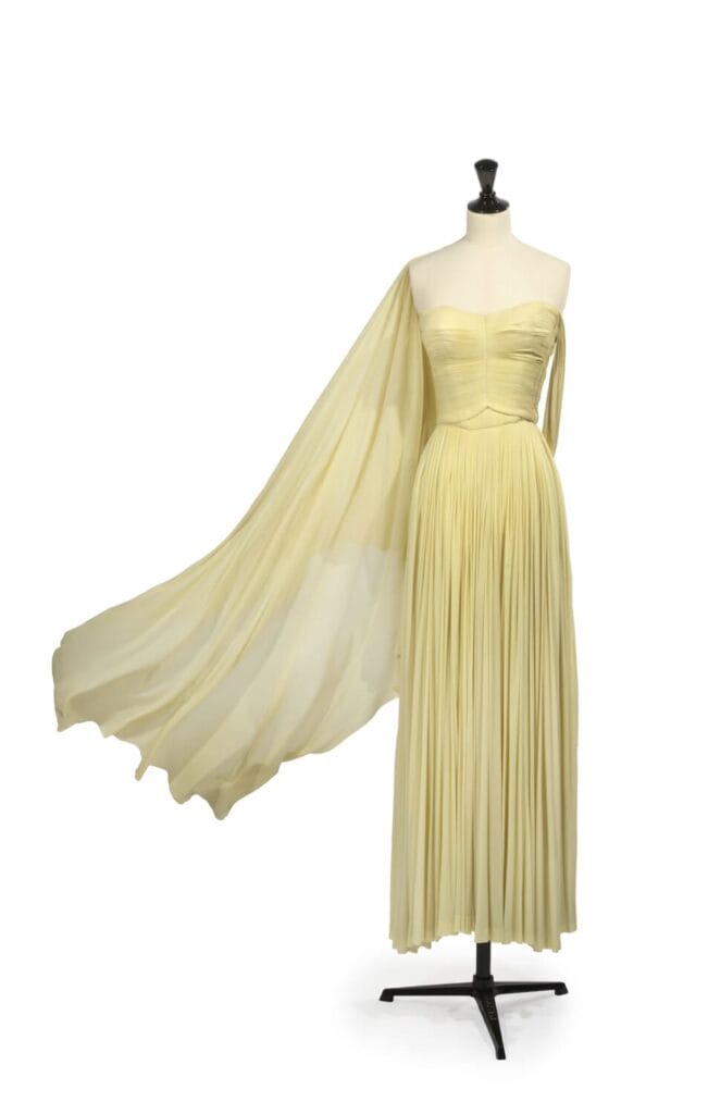 Grès, collection Haute Couture, circa 1955 Prototype du défilé  Robe du soir longue, haut bustier plissé, jupe fluide et panneau faisant étole, jersey de soie jaune paille. Griffe noire, graphisme blanc « Grès 1 rue de la Paix Paris - Made In France « - Plomb de douane  Provenance: Archives personnelles d’Alix Grès  - Collection maison Jacques Esterel. - Collection Quidam de Revel.   Exposition: Madame Grès, entre Ombre et Lumière, Bourgoin-Jallieu du 19 juin 2004 au 31 janvier 2005 2 000 - 3 000 euros