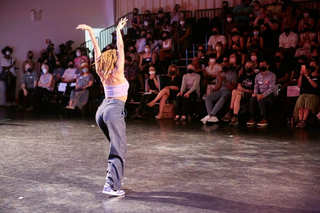 Image of two speakers and an ASL interpreter at the Dance. Workforce. Resilience.
(DWR) Initiative Launch Event on July 20, 2022 at Mark Morris Dance Center. The photo is
t
aken behind the speakers, and in the background, attendees sit in bleacher seating.